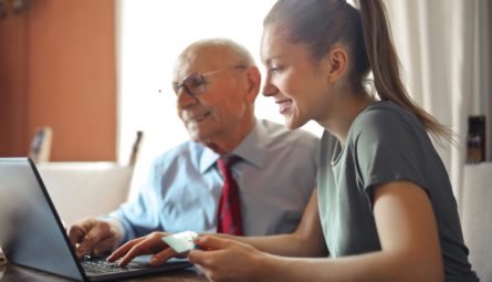 lady helping elderly gent to use a laptop