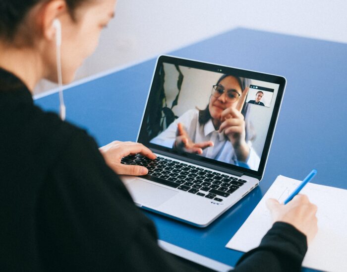 woman listening to a zoom session on her laptop and taking notes