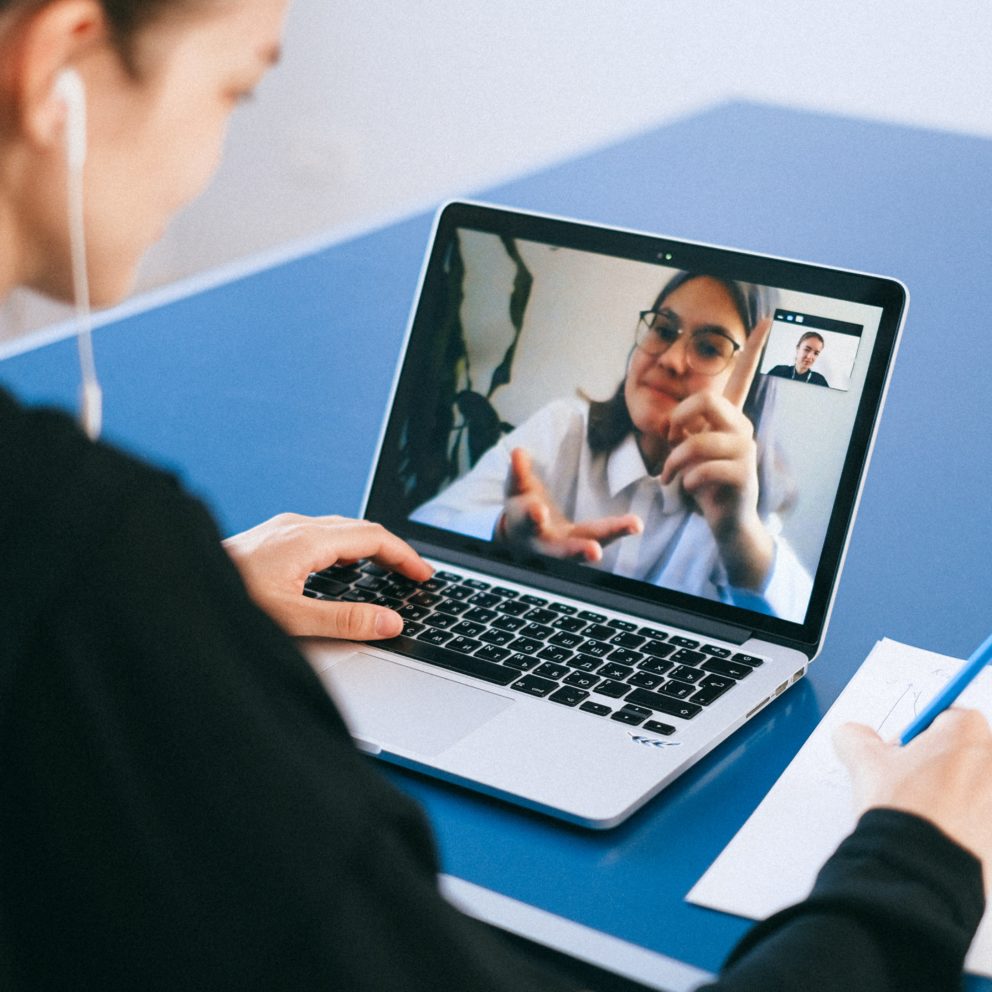 woman listening to a zoom session on her laptop and taking notes