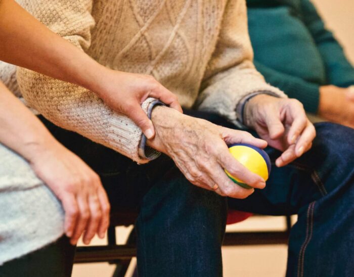 A woman laying a caring hand on the arm of an elderly person who is sitting beside her