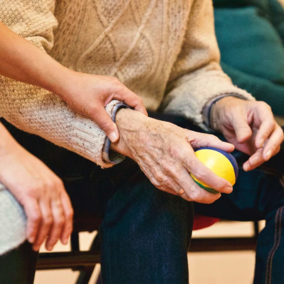 A woman laying a caring hand on the arm of an elderly person who is sitting beside her