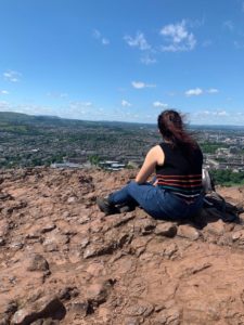 Zein at the top of Arthur's Seat. She is sitting with her back to the camera looking out over the view of Edinburgh.