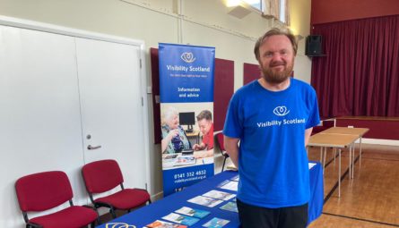 Visibility Scotland staff member, Craig, standing in front of an information table. There are leaflets about local services on the table.