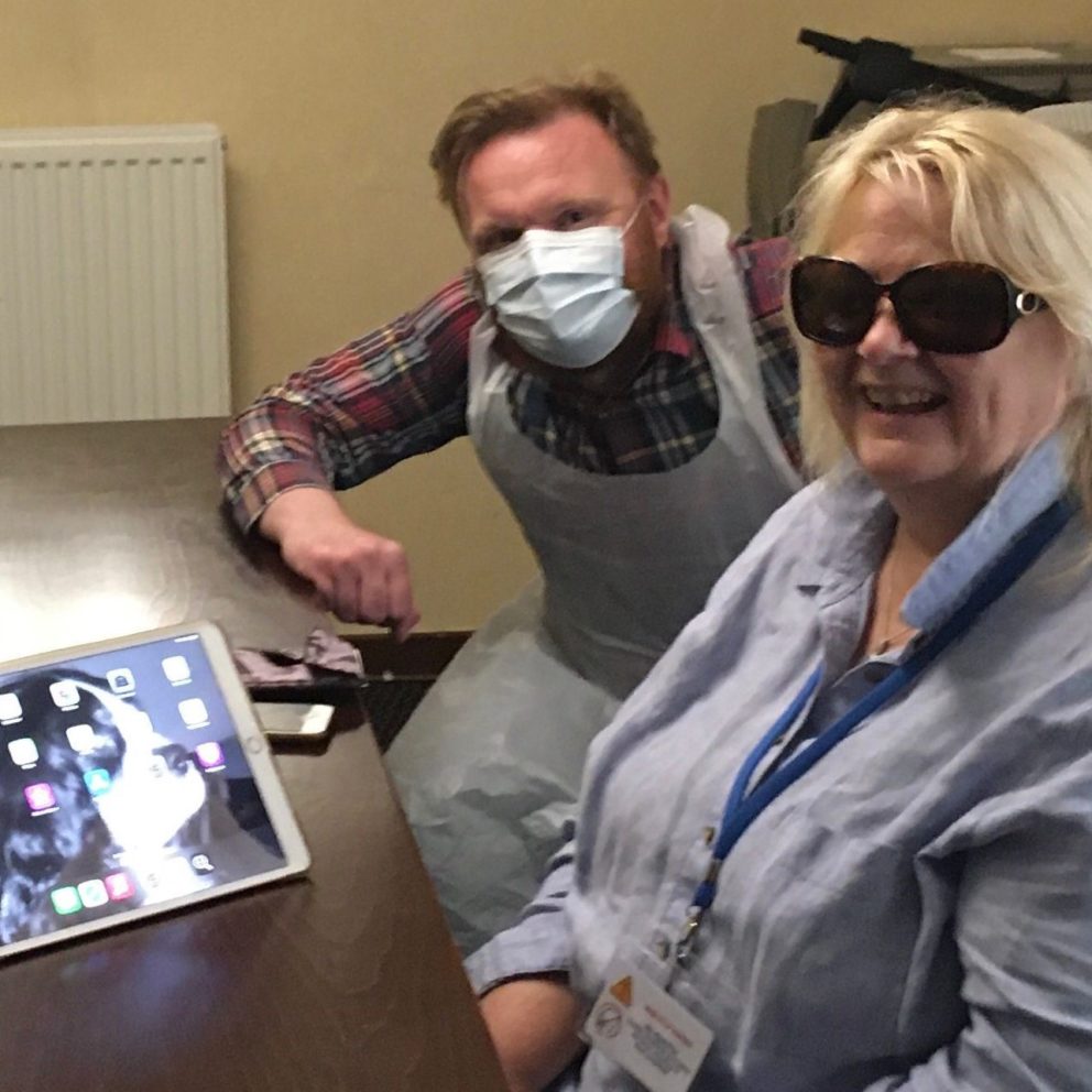 A woman wearing dark glasses sitting at a table with a member of staff from Visibility Scotland. There is an iPad and iPhone on the table.