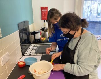 An EyeCan! course participant preparing stuffed peppers in the Visibility Scotland kitchen, assisted by a Visibility Scotland staff member.