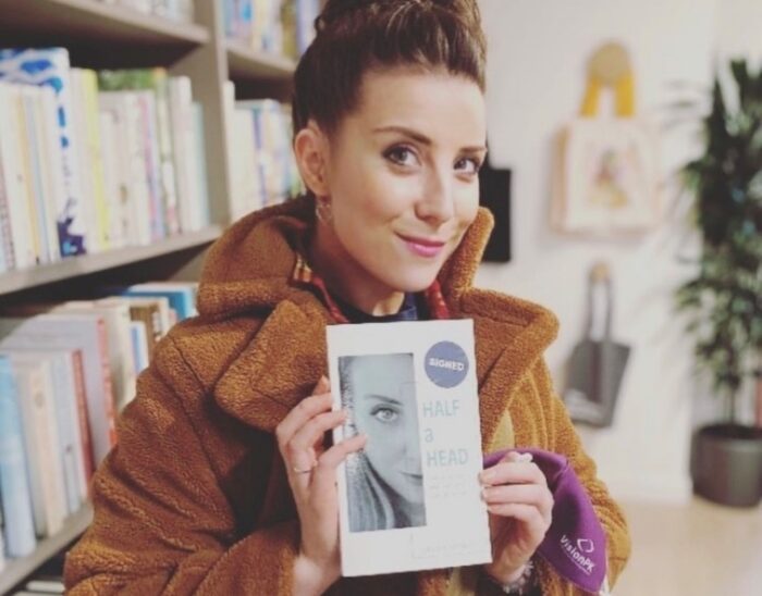 Gemma smiling and holding a copy of her book "Half a Head"