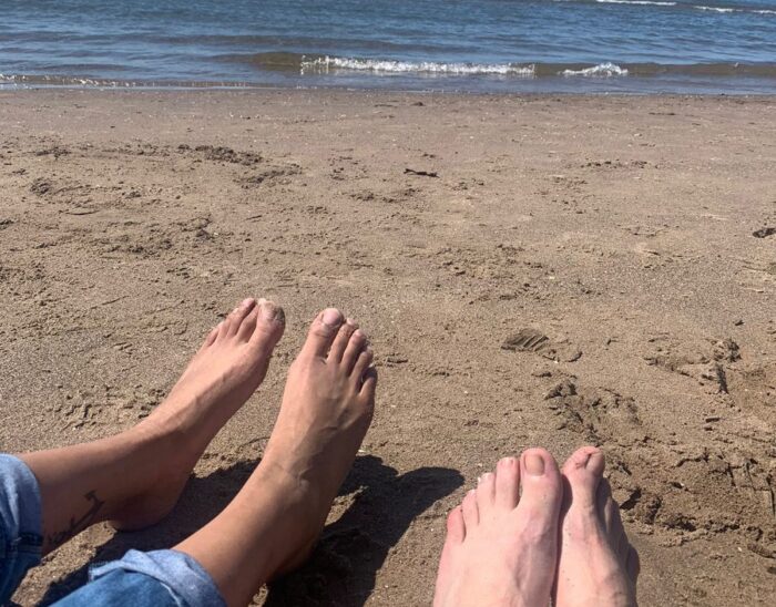 A view from a beach overlooking the sea. There are two pairs of feet visible, both without shoes and socks.