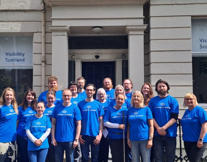 the staff team gathered outside Visibility Scotland's office. The team are smiling and wearing blue Visibility Scotland t-shirts