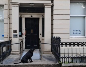 Bolt, a black gun dog, sits outside the main entrance to our office