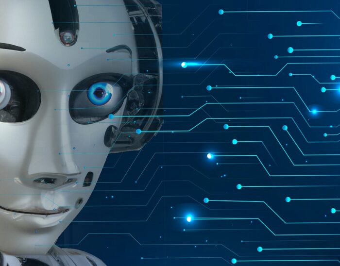 A robot head with human looking eyes smiles at the viewer. The background in blue and there are light coloured lines representing electrical paths going into the robot's head.