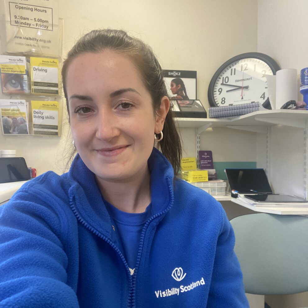 Miriam sits in our patient support room at Gartnavel General Hospital. Miriam is wearing a blue Visibility Scotland fleece and t-shirt and is smiling.
