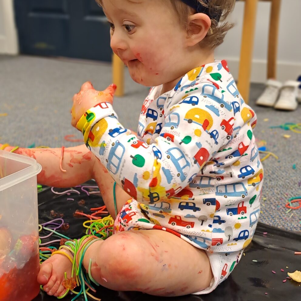 A toddler sits on the floor while playing with colourful string.