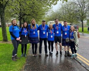 a group of eight fundraisers huddle with their arms round one another in Glasgow Green. They are wearing blue Visibility Scotland t-shirts.