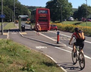 A rural road on a sunny day with a cycle track running behind a bus stop