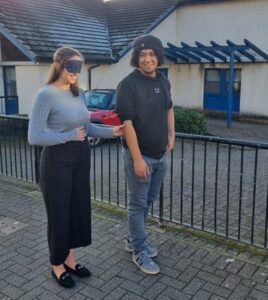 A person in a blindfold being guided by another person.