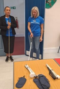 Visibility Scotland staff members Jeni and Audrey stand next to each other. Jeni is teaching use of the long cane.