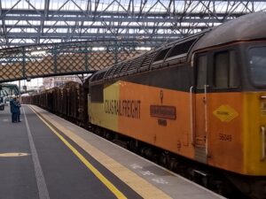 a freight train with a yellow and orange front car with the words "Colas Rail Freight" printed on it