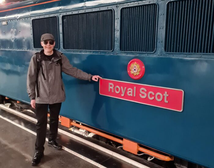Roy standing in front of a Royal Scot train car, he is smiling