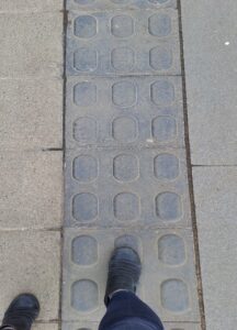 A pair of feet walking across lozenge paving. The lozenge elements are arranged in a two by three grid in each paving stone.