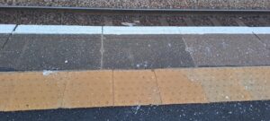 Offset blister paving near the edge of the platform in a train station.