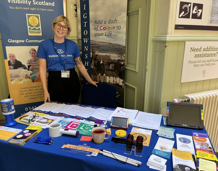 A person in a blue Visibility Scotland top stands behind a table smiling.