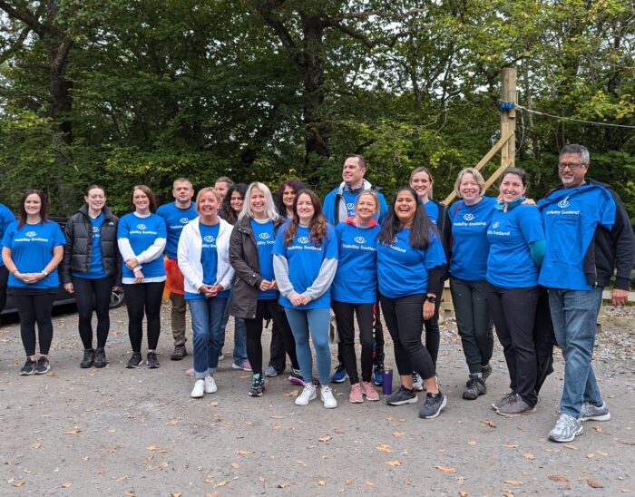 A group of people stand together smiling and wearing blue branded Visibility Scotland tops
