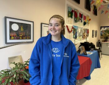 A person wearing a blue branded Visibility Scotland top and fleece smiles at the camera.