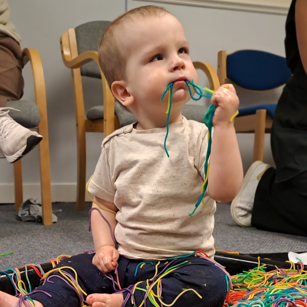 A child plays with brightly coloured string-like objects.