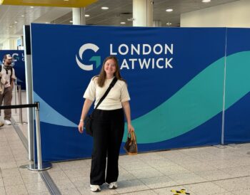 Person smiles standing next to blue sign that says London Gatwick in white writing