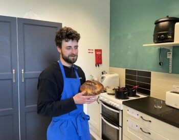 A person wearing a blue apron holding a loaf of bread.