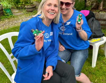 Two Visibility Scotland staff members sit together smiling and playing bells.
