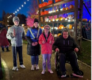 Four people pose together while smiling in front of a carved pumpkin exhibit. 