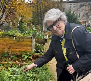 Jent smiles while picking herbs in a garden.
