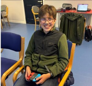 A smiling young person holding a Nintendo Switch controller controller. 