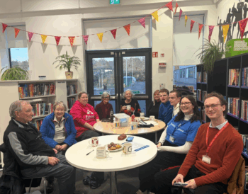 A group of people sit around two tables with snacks. Everyone is smiling.
