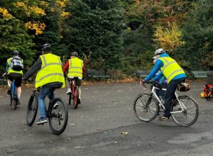 A group of people riding bicycles in a park wearing hi-vis vests and helmets