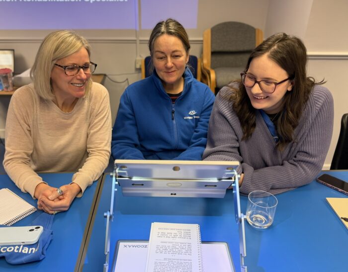 Three people smile while using an electronic magnifier to read a document