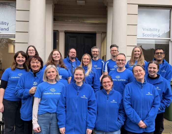 The Visibility Scotland staff team stands outside the main office building smiling.