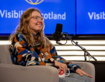 A person sits in a podcast studio smiling.