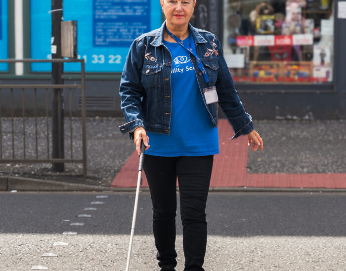 A person using a guide cane walks confidently across a road.