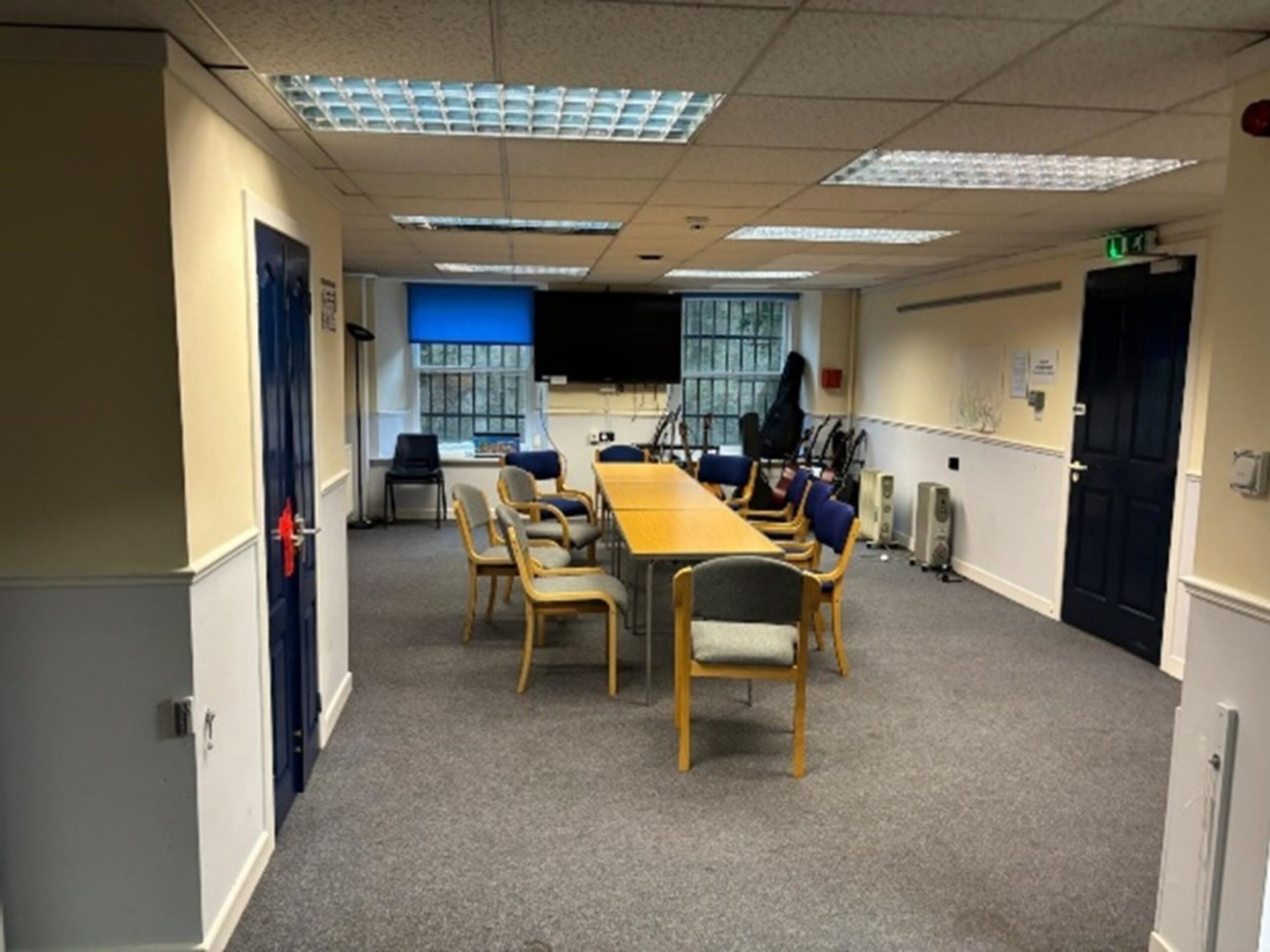 A basement room with 10 chairs around two tables. There is a TV on the back wall.