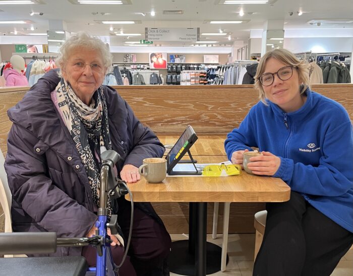 Two people sit at a table smiling at the camera. In between them is a digital magnifier.
