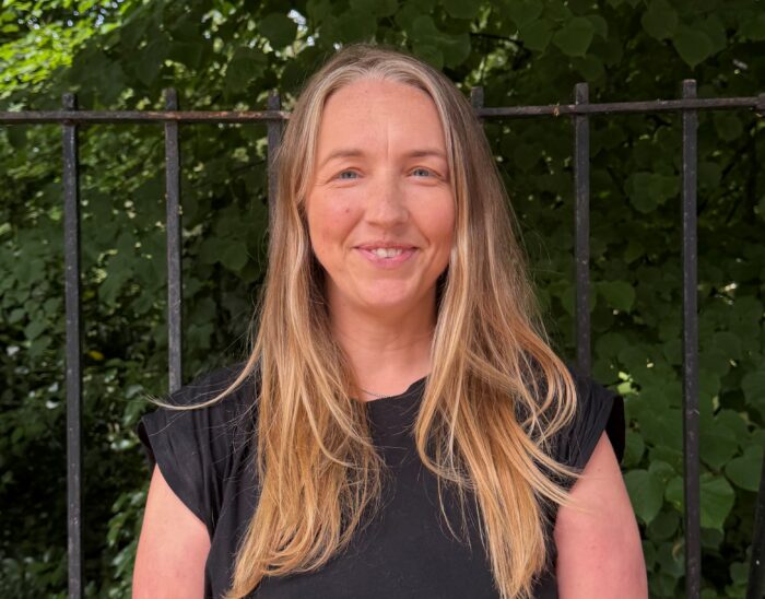 Laura Walker, CEO, stands outside smiling. She has long blonde hair and is wearing a black top.