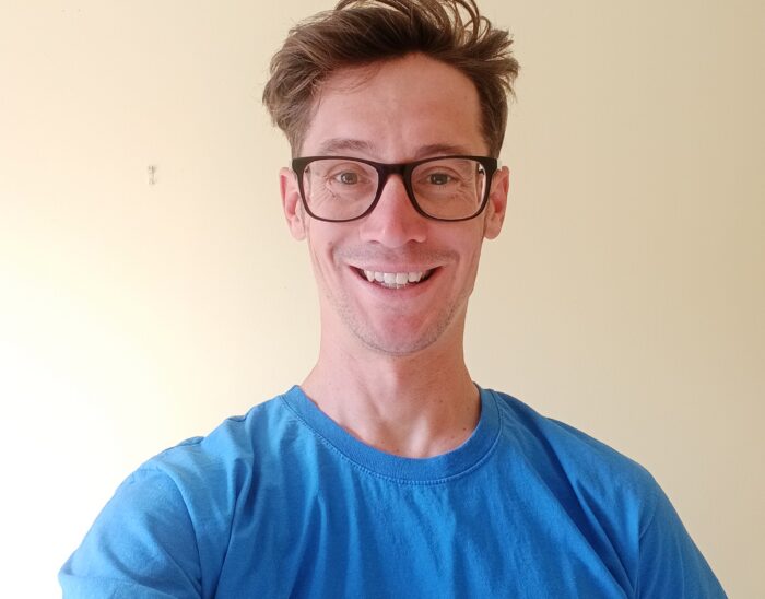 Josh smiles at the camera. He is wearing a blue Visibility Scotland top and black glasses.